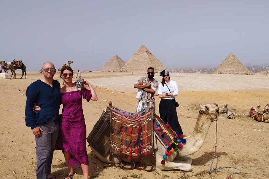 A group of friends smiling and posing cheerfully with camels in front of the majestic Giza Pyramids, indicating a fun and memorable tour experience