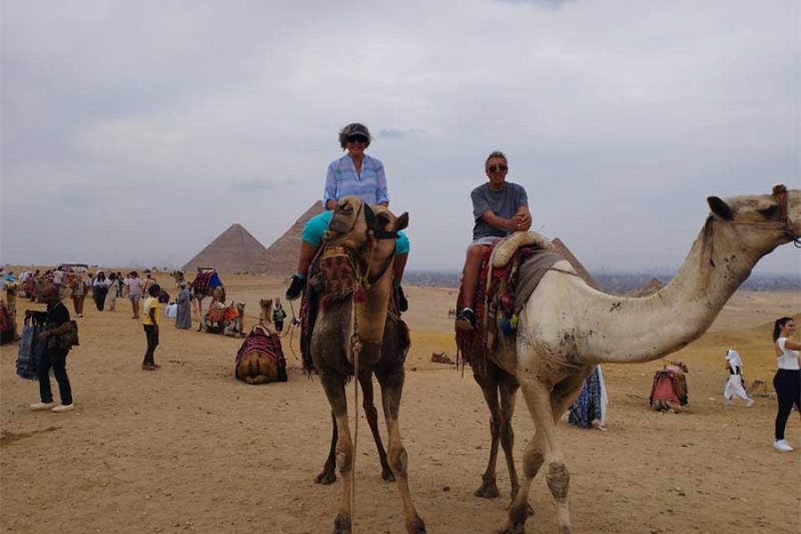 A couple riding camels together across the Giza Pyramids Plateau, with the majestic pyramids clearly visible in the background