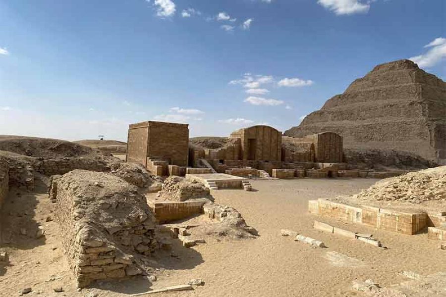The ancient, stepped silhouette of the Djoser Pyramid (Step Pyramid) at Saqqara, surrounded by its vast complex of ruined temples and courtyards