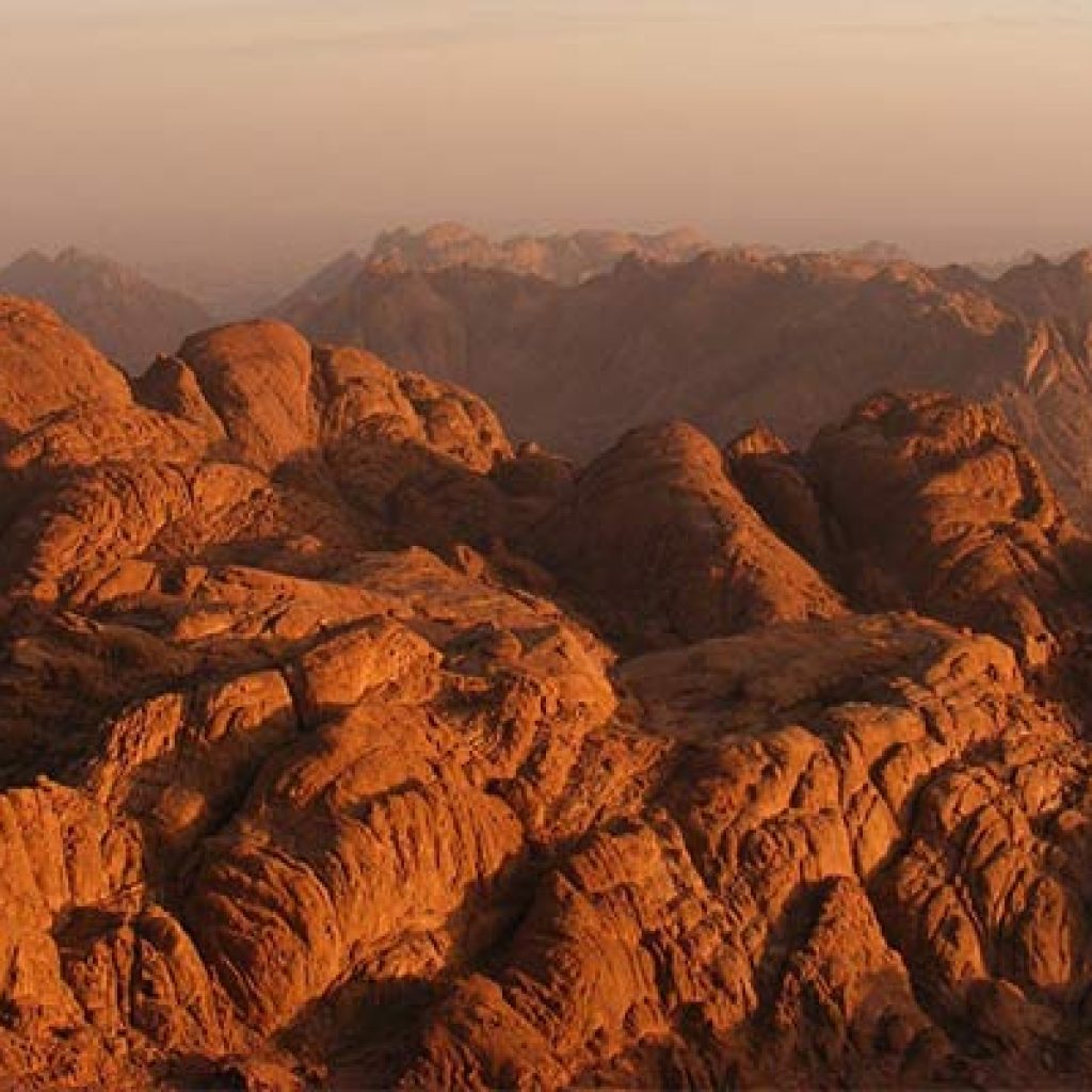 reddish-brown granite peaks of Mount Sinai (Gabal Musa), showing its barren and dramatic desert landscape under a vast sky, evoking its spiritual significance