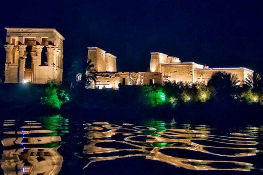 Philae Temple, dramatically illuminated with colorful lights during its evening Sound and Light Show, casting vibrant reflections on the calm waters of the Lake Nasser surrounding the island