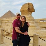 A couple posing affectionately in front of the majestic Great Sphinx of Giza, with the ancient monument and a clear sky forming a classic romantic backdrop