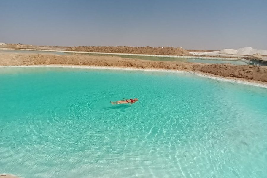 A client effortlessly floating on the highly buoyant, crystal-clear waters of a salt lake in Siwa Oasis