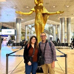 Trois voyageurs souriants posent devant une statue dorée de la déesse égyptienne Hathor à l’aéroport du Caire.