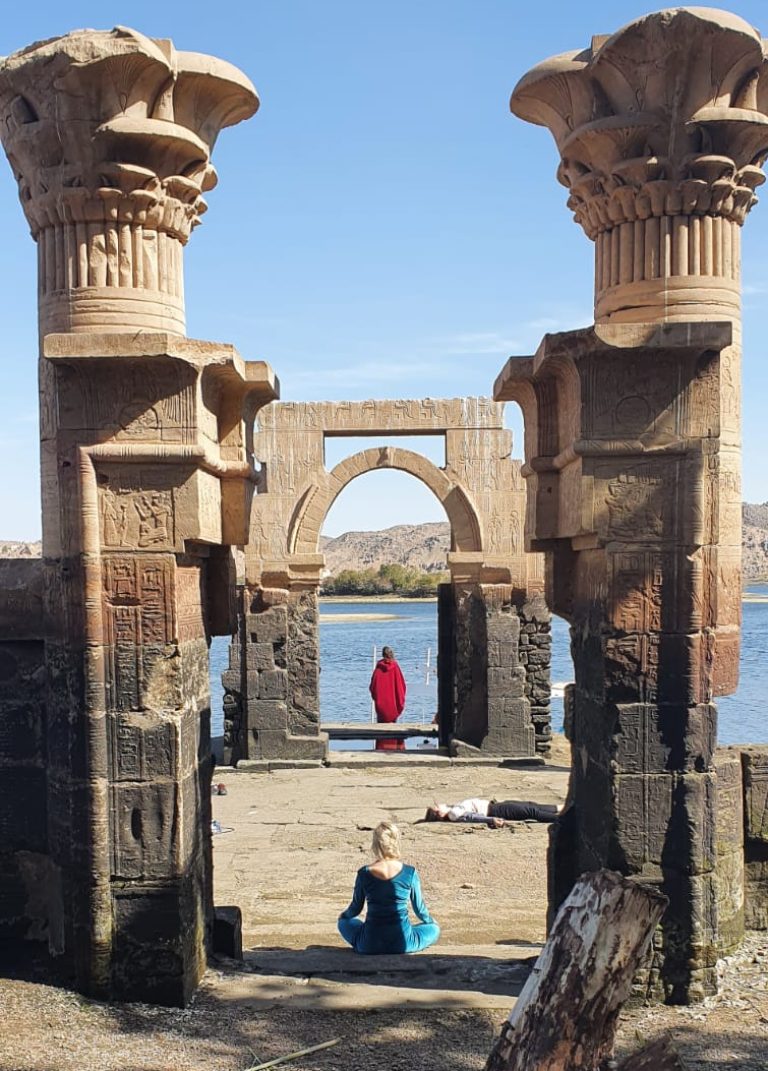 Des clients en position de méditation dans l'enceinte sereine du Temple de Philae à Assouan, entourés d'anciennes colonnes et des eaux calmes du Nil