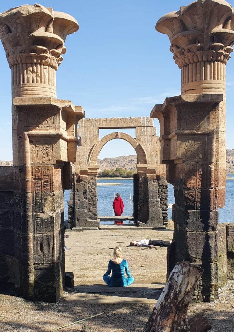 Clients sitting in a meditative pose within the serene grounds of Philae Temple in Aswan, surrounded by ancient columns and the calm waters of the Nile