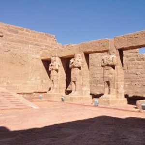 Sur la photo, un magnifique temple d'Assouan : il y a une grande cour avec quatre statues debout et une porte sur le côté pour entrer dans le temple.