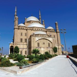 Mosquée imposante avec plusieurs dômes blancs et deux minarets, sous un ciel bleu clair.