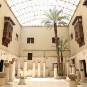 Cour intérieure d’un site islamique avec colonnes anciennes, palmiers et fenêtres en bois sculpté.