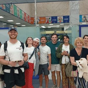 Un groupe de neuf personnes, hommes et femmes d'âges variés, posent pour une photo à l'intérieur de l'aéroport.