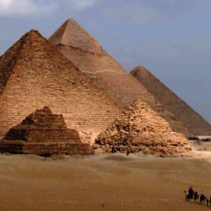 Vue panoramique des pyramides de Gizeh en Égypte, avec des chameaux traversant le désert au premier plan.