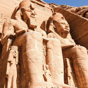 Deux des quatre colosses monumentaux de Ramsès II sont représentés, taillés dans la façade rocheuse du grand temple d'Abou Simbel. Les statues sont assises et portent la double couronne de l'Égypte. De plus petites figures, représentant des membres de la famille royale, se trouvent à leurs pieds. La lumière du soleil met en évidence les gravures et les détails usés par le temps.
